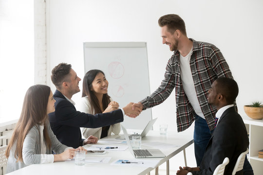 Smiling businessman handshaking welcoming new member at multiracial team meeting, friendly partners greeting start or finish negotiations shaking hands thanking for help, respect and first impression
