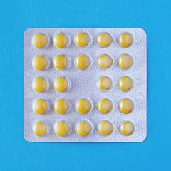 Yellow round pills in a blister on a turquoise background (square image format)