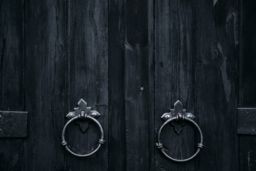 Old black wooden door with ring doorknobs. Close up view, texture, pattern