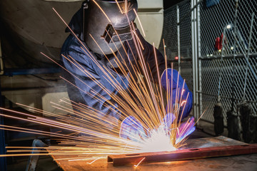 Industrial worker is welding automotive part in factory