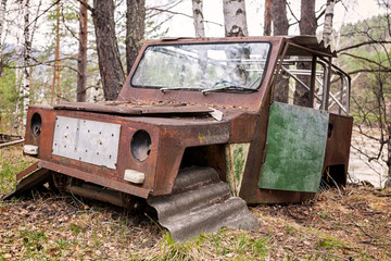 Close-up of an old rusty jeep car with a broken door and no wheels on the background of a green coniferous forest