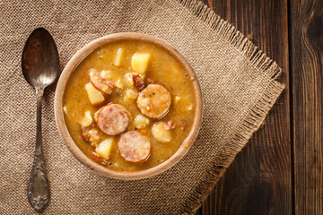 Wooden bowl of split pea soup with sausage and potatoes
