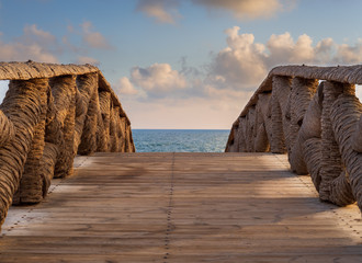 Wooden bridge made of palm trunks leading to the sea coast with partly cloudy sky in sunrise time...