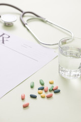 Stethoscope, pills and glass of water on light green background. medicine concept