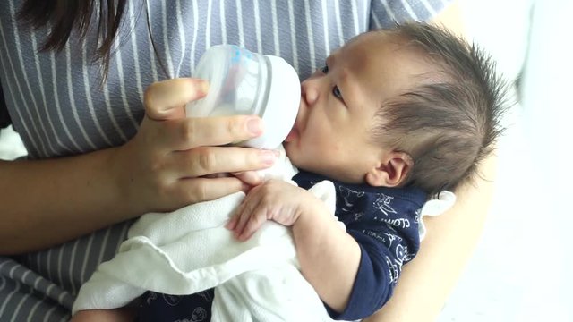 Mother feeding the baby with baby bottle in the living room