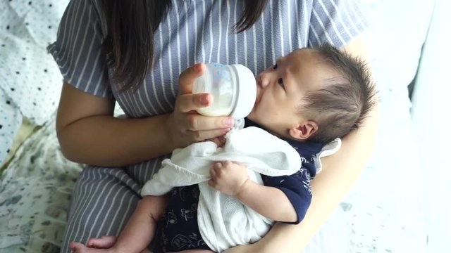 Mother feeding the baby with baby bottle in the living room
