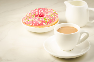 Obraz na płótnie Canvas white cup coffee with milk and fresh sugary pink donut/white cup coffee with milk and fresh sugary pink donut on a white marble background. Selective focus and copyspace