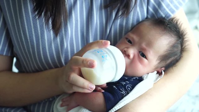 Mother feeding the baby with baby bottle in the living room
