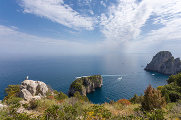 Fototapeta na wymiar Capri Italy, island in a beautiful summer day, with faraglioni rocks and boat crossing the bay.