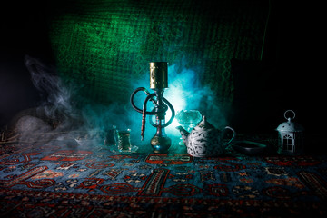 Hookah hot coals on shisha bowl making clouds of steam at Arabian interior. Oriental ornament on the carpet eastern tea ceremony. Stylish oriental shisha in dark with backlight.