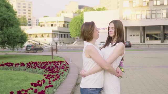 Mother and adult daughter laughing and chatting in the park on a sunny day. Attractive Brunette is Hugging Her Mom with Love and Tenderness
