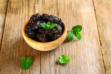 Prunes with mint leaves in a bowl on an old wooden table.