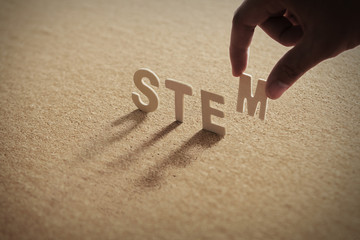 STEM wood word on compressed or corkboard with human's finger at T letter. © phloxii