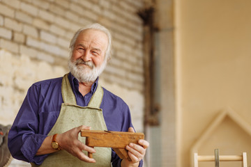 cheerful pensioner is holding wooden plane for working with wood