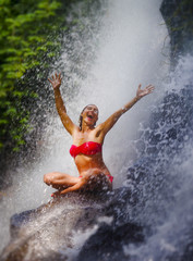 young attractive and happy woman with fit body practicing yoga wet under tropical paradise waterfall stream screaming excited with opened arms