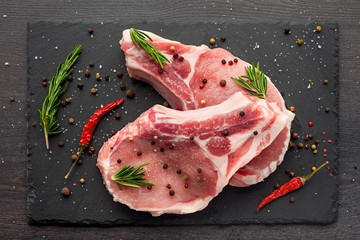fresh raw meat with spices and rosemary and red pepper on black slate, on dark background, pork,...