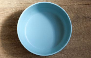 Empty blue plastic bowl on wooden background, above view