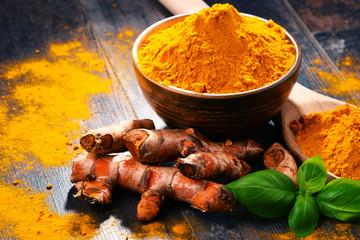 Composition with bowl of turmeric powder on wooden table