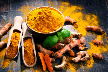 Composition with bowl of turmeric powder on wooden table