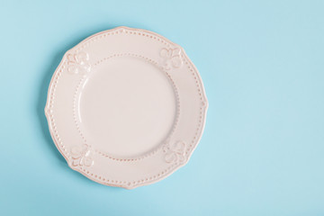 White rustic plate on light blue pastel background. Plate on the left side of frame. Top view.