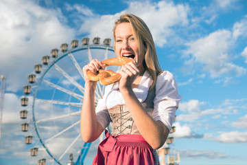 young sexy woman is doing oktoberfest in munic summer, spring folk festival she is wearing a dirndl and holding a hear brezn in her hand