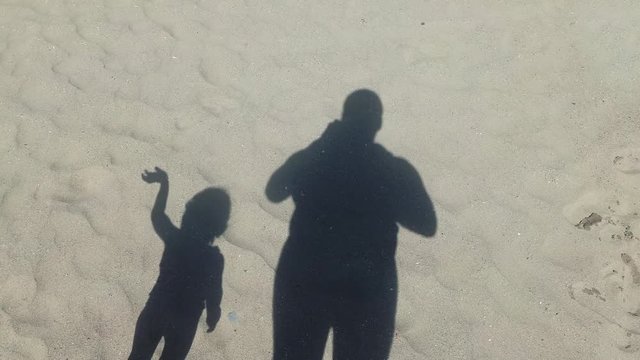 Shadow of a man and a kid on sandy background, waving