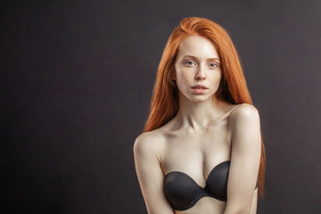 Slim young girl with long gorgeous red hair and strapless bra on black background with copyspace . Healthy Hair and Skin Care