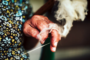 Closeup of fingers of a old woman is making yarn for knitting from natural rough sheep wool (natural fiber) on traditional way