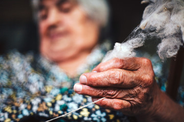 Closeup of fingers of a old woman is making yarn for knitting from natural rough sheep wool (natural fiber) on traditional way