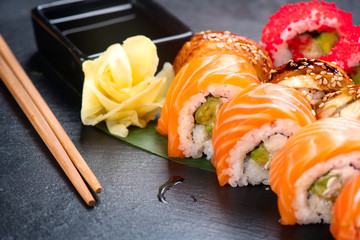 Sushi rolls closeup. Japanese food in restaurant. Roll with salmon, eel, vegetables and flying fish caviar on black slate background