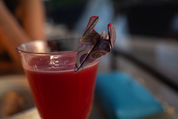 Bright red drink in a glass with a paper plane origami as decoration