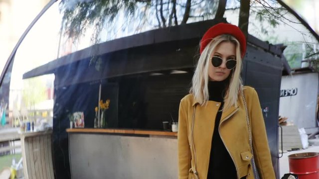 outdoors mirror reflection of cool confident fashion woman looking at camera corecting blonde hairstyle and smiling pretty female person wearing sunglasses jacket and hat wind blowing sunny day