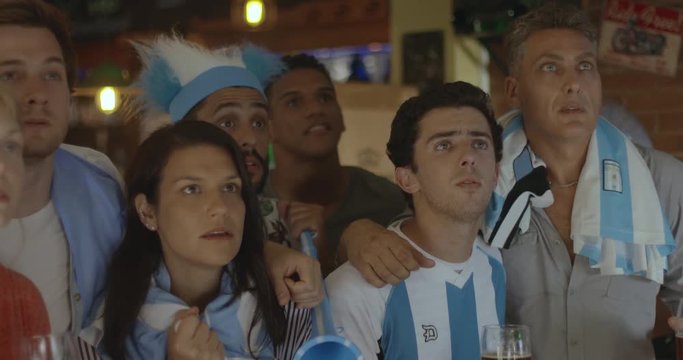 Argentinian football fans celebrating victory while watching televised match in bar, slow motion