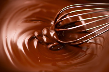 Chocolate. Mixing melted dark chocolate with a whisk. Closeup of liquid hot chocolate swirl....