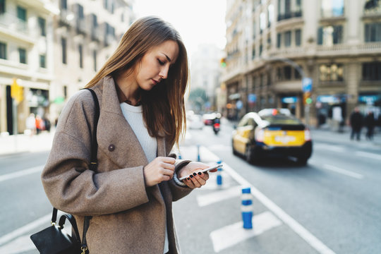 Successful designer reading email on  mobile phone connected to wifi while walking the street. Charming student girl wearing stylish clothes searching information in the internet on a smartphone.