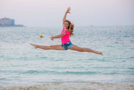 Cute young girl doing split-jump at the beach