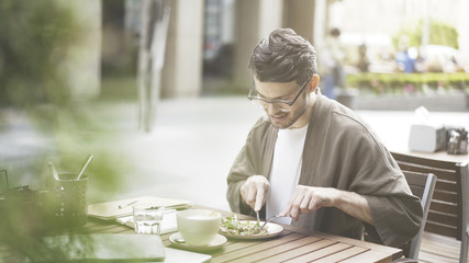 A handsome bearded man in eyeglasses eating fresh salad at cafe outdoors alone