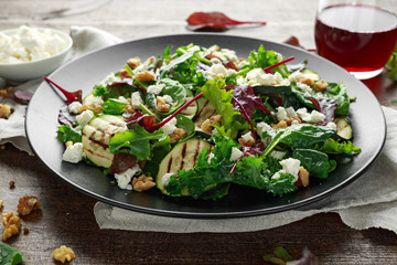 Grilled Zucchini salad with feta cheese, walnut nuts and glass of red wine in a black plate on wooden table