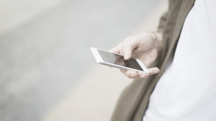 A closeup of white phone, a man holding a white smartphone on the street outdoors