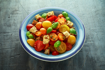 Panzanella Tomato salad with red, yellow, orange cherry tomatoes, capers, basil and ciabatta croutons. summer healthy food.