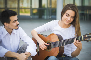 Young girl playing guitar and her male friend listening