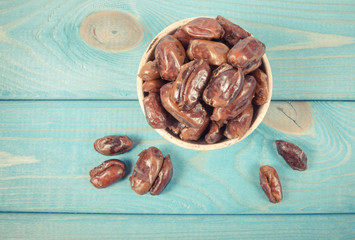 Dry dates fruit in the bowl, on the wood background.