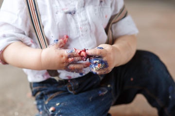 One year old kid after eating a slice of birthday smash cake by himself getting dirty. Close up shot of hands