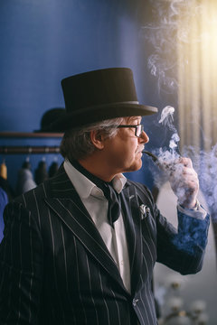 Portrait Of Posh Chic Virile Millionaire Or Rich Mature Man Visiting A Luxury Fashion Boutique For Buing New Exclusive Suit, Smoking Tobacco Pipe Breathing Out Cloud Of Smoke