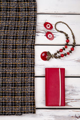 Female warm skirt and colorful accessories. Red purse and jewelry on white wooden background. Women stylish essentials.