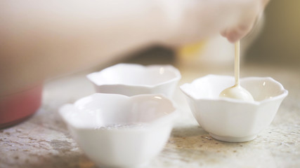 A woman is decorating sweets pour white chocolate cream on a sweet