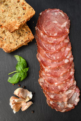 Salami smoked sausage slices basil leaves and peppercorns on black stone background