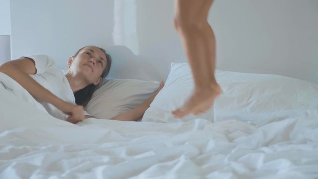 Little girl jumping on bed and wakes up her young mother in the early morning