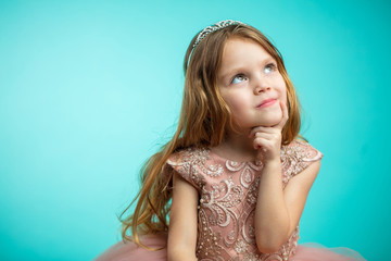Portrait of adorable 4- year old girl with long blonde loose hair in pink princess dress looking up aside with dreamy expression isolated over blue background with copyspace for text. © alfa27