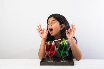 Cute asian/Indian little girl posing with cold drink or fresh juice at table over white background
